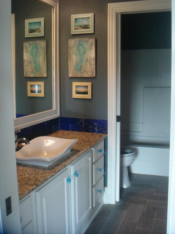 Ceramic tiles that mimic wooden planks, a wavy sink, and ocean blue tiled backsplash make this bathroom feel like a walk at the beach